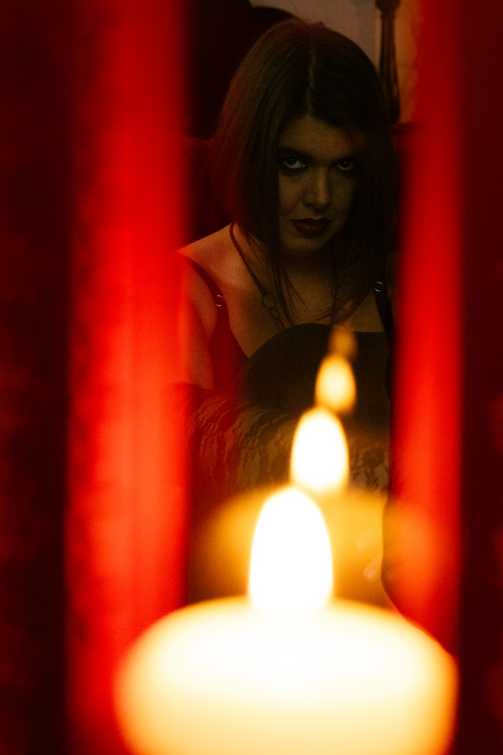 Reflected candle flames lead back through red curtains to a sultry brunette.