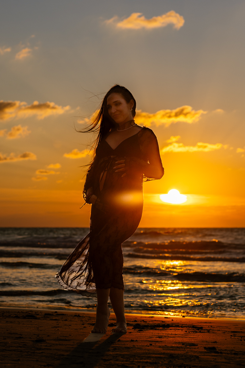 Lovely pregnant woman on the beach at sunset, the rays of the sun kissing her baby bump.